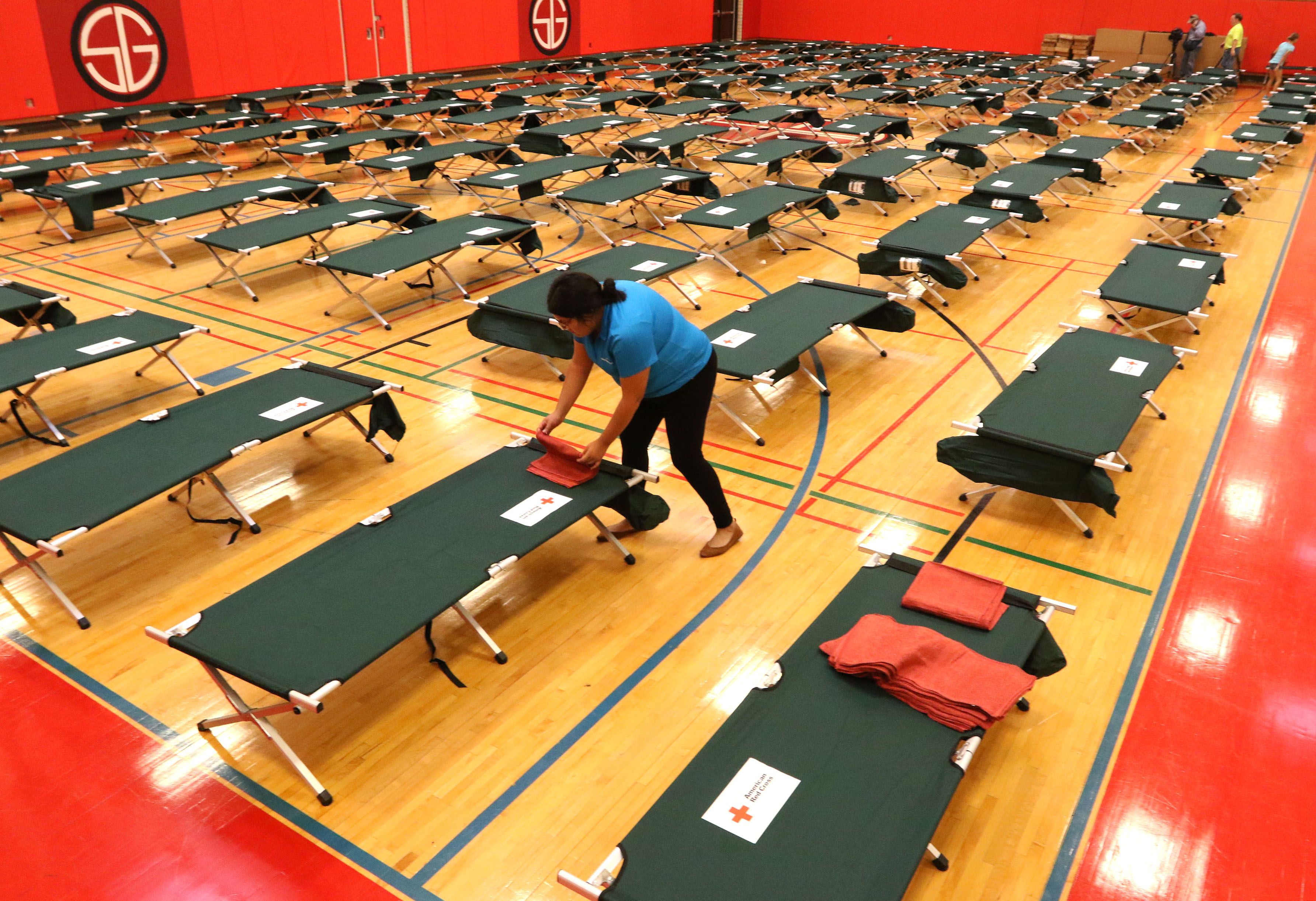 Margarita Faz, a Dallas Park and Recreation employee, folds a towel on a cot on Sunday afternoon on the Samuell Grand Recreation Center's gym floor. The American Red Cross and the city of Dallas opened a third shelter for Hurricane Harvey evacuees at the recreation center at 6200 E. Grand Ave.(Irwin Thompson/Staff photographer)