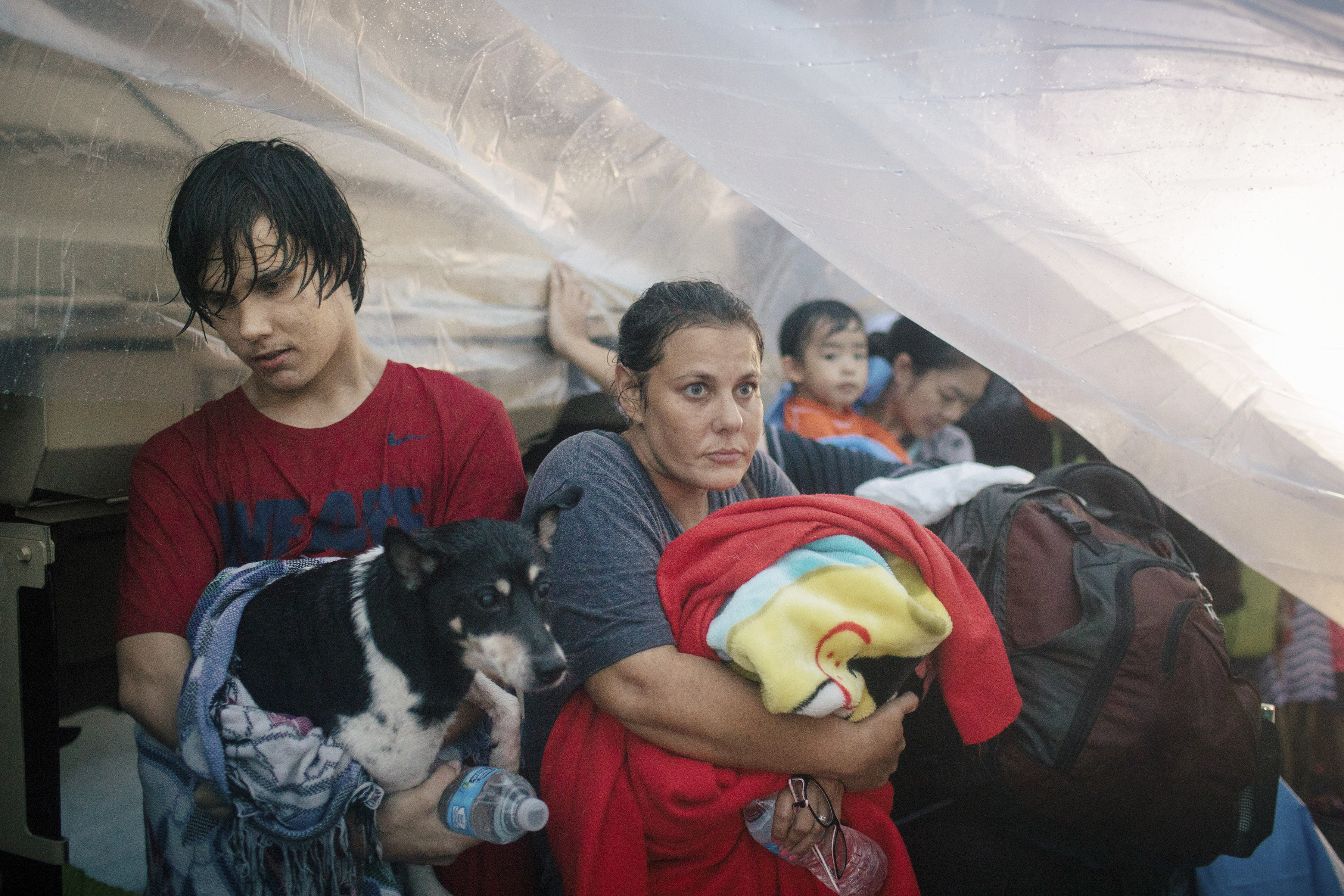Sherri Thomas, her son Brandon, 17, and their dog Jaba sit under a tarp while waiting to be bused to a shelter in Houston's Meyerland area, where floodwaters were above some rooflines, Aug. 27, 2017.&nbsp;(ALYSSA SCHUKAR/NYT)